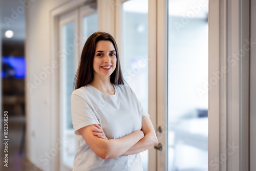 Smiling woman with arms crossed stands near glass doors in a modern indoor space during daytime Free Download Smiling woman with arms crossed stands near glass doors in a modern indoor space during daytime - GFXLoad