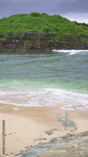A pristine and beautiful tropical beach with stunning panoramic views on the southern tip of Java, Indonesia. The landscape of this hidden beach features clear blue skies, white sand, and big waves.