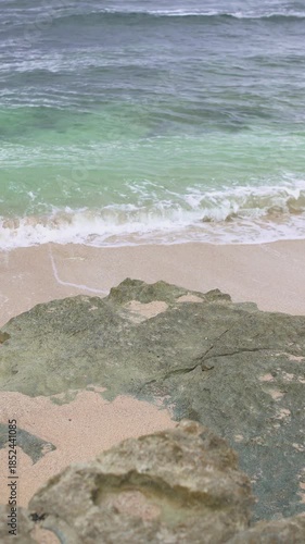 A pristine and beautiful tropical beach with stunning panoramic views on the southern tip of Java, Indonesia. The landscape of this hidden beach features clear blue skies, white sand, and big waves.