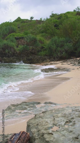 A pristine and beautiful tropical beach with stunning panoramic views on the southern tip of Java, Indonesia. The landscape of this hidden beach features clear blue skies, white sand, and big waves.