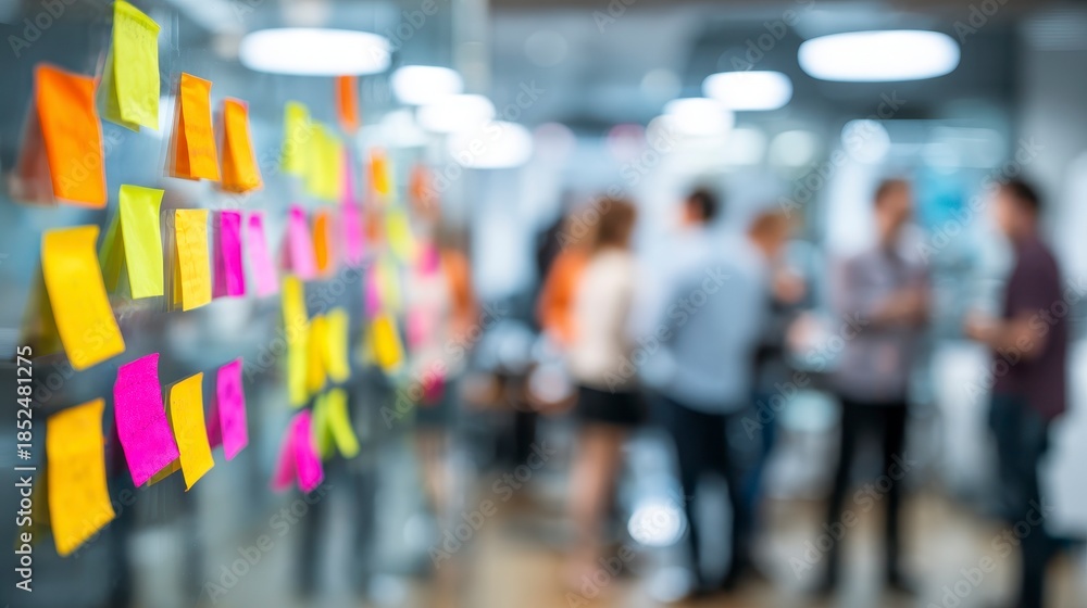 Fototapeta premium Focus on colorful sticky notes on a glass wall in an office, with blurred people in the background, a modern workspace