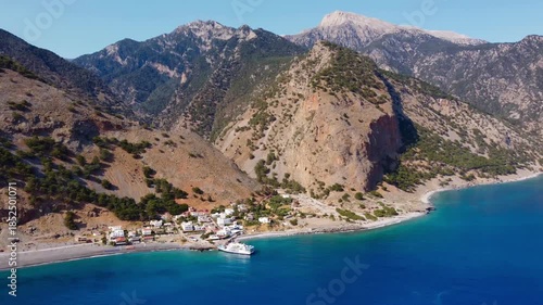 Aerial footage of the ferry at Agia Roumeli, and the final valley at the end of the Samaria Gorge hike. Crete's White Mountains tower above deep blue waters of Libyan Sea - Crete, Greece