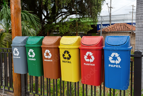 Row of brightly colored recycling bins in Portuguese (Lixo Comum, Vidro, Organico, Metal, Plastico, Papel) mounted on a fence in the city of Miranda, Mato Grosso do Sul, Brazil.