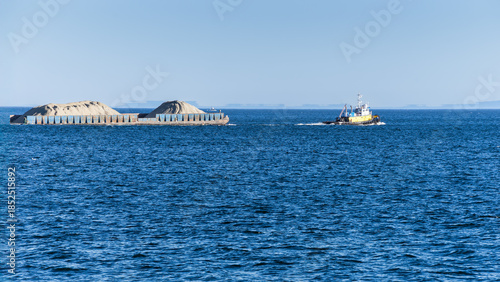 Tugboat  is pulling a barge of ore in open sea water