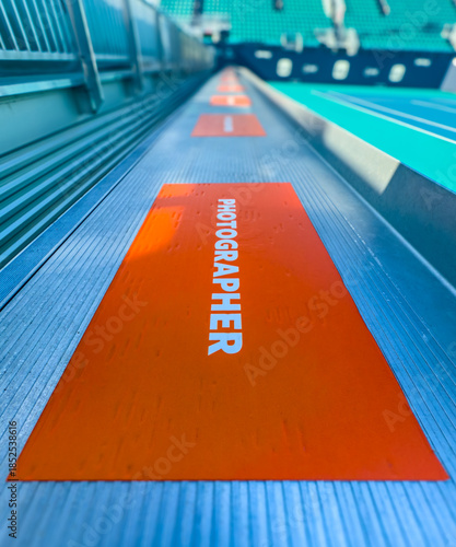 Orange sticker marking the photographers’ zone at a tennis court, designating a reserved area for sports media and event photography.