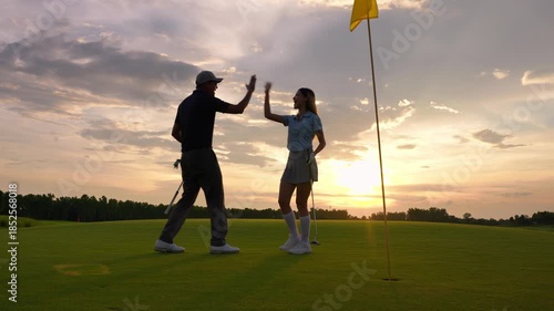 Asian man and woman golfers swing clubs together on scenic golf course. 