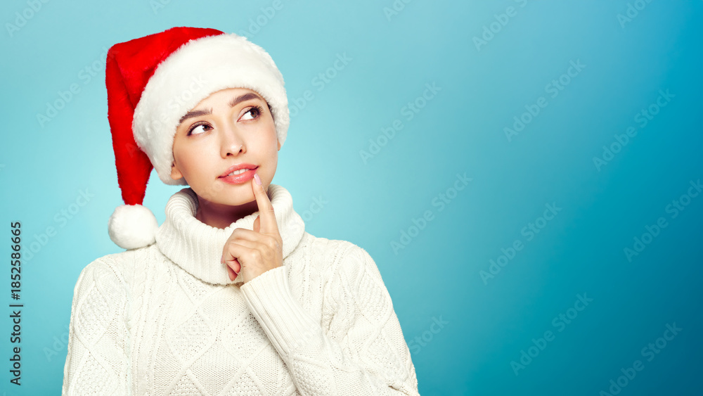 Fototapeta premium Beautiful woman in a white knitted sweater and santa hat isolated on a blue background. Christmas or New Year festivities. Holiday and Party