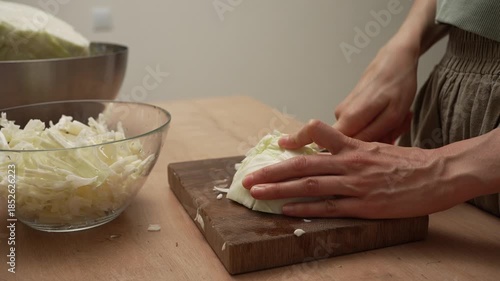 Close-up shot of a chef expertly slicing a crisp white cabbage on a wooden cutting board, carefully preparing the raw vegetable for a nutritious salad in a cozy home kitchen setting