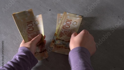 Close-up of a pair of hands holding a stack of Canadian $100 bills, then putting the money down to count each bill one by one.