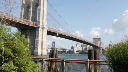 Brooklyn Bridge and Manhattan Bridge from Downtown, New York City, United States. Esplanade park. American architecture, famous tourist landmark. Waterfront urban promenade. Old wooden pier piles.