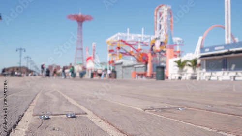 Coney Island beach promenade in Brooklyn, New York, United States. Wooden boardwalk near retro luna park. Amusement park on ocean coast beach. Waterfront summer holiday, people walking on promenade.