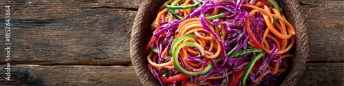 A vibrant Asian noodle salad with fresh carrots, crisp cucumber, and shredded red cabbage is presented in a rustic bowl against a dark wood surface.