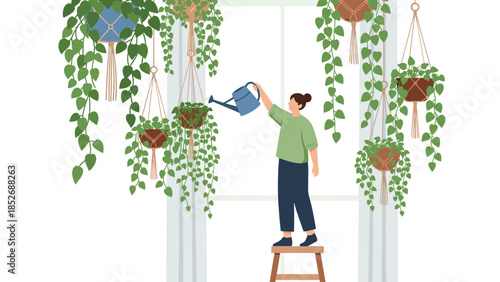 A woman standing on a stool to water a variety of lush green hanging plants in macrame hangers near a large, bright window at home.