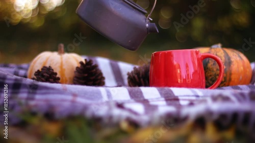Woman enjoying autumn picnic pouring tea from kettle 