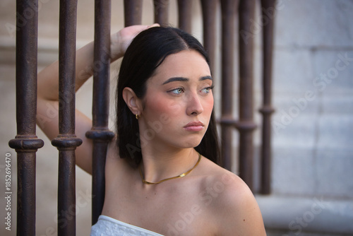 Cuadro en lienzo Portrait of a young, beautiful, dark-haired, blue-eyed Hispanic woman with a sad and worried look, clinging to a fence, representing the oppression of women