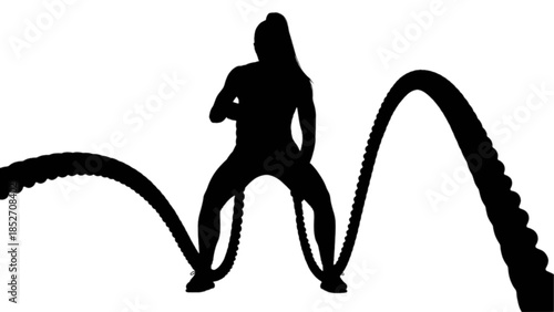 A focused woman powerfully exercises with battle ropes in a fitness studio.