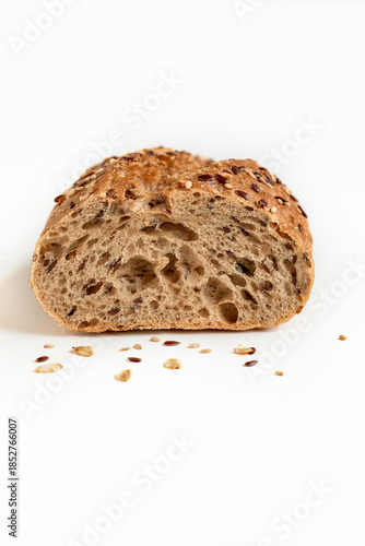Whole grain baguette cut with different seeds lying on a white table, isolated