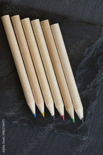 Group of colored wooden pencils lying on f two different grey stone texturs with varying degrees of roughness and layering.
