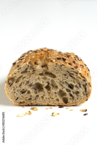 Macro photo of whole grain baguette cut with different seeds lying on a white table