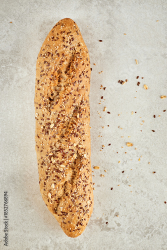 Closeup shot of whole grain baguette  with different seeds lying on a grey table