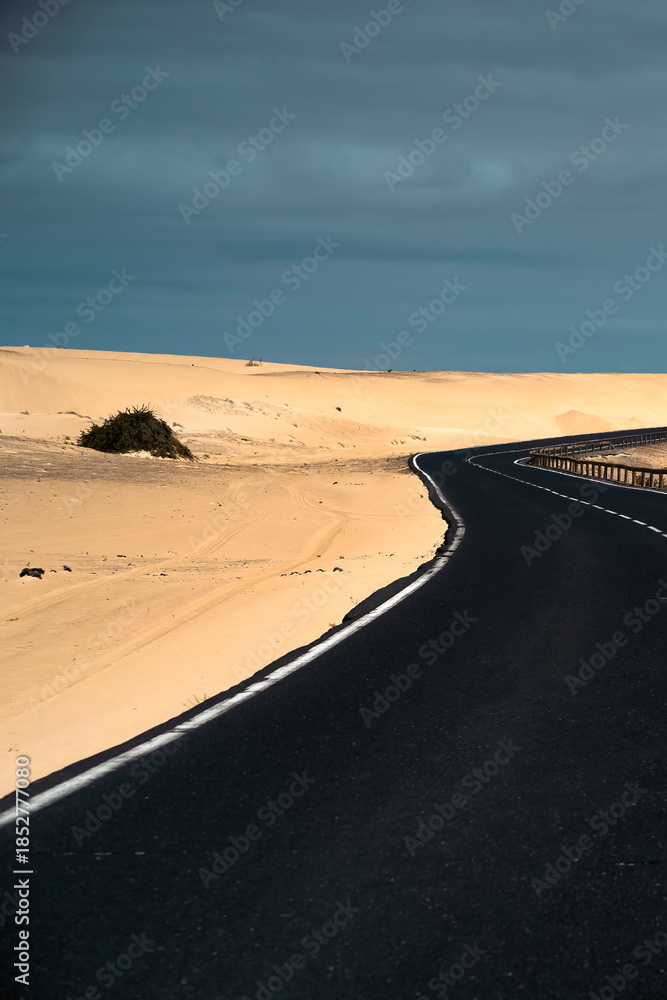 Fototapeta premium An asphalt road among desert with sandy dunes.