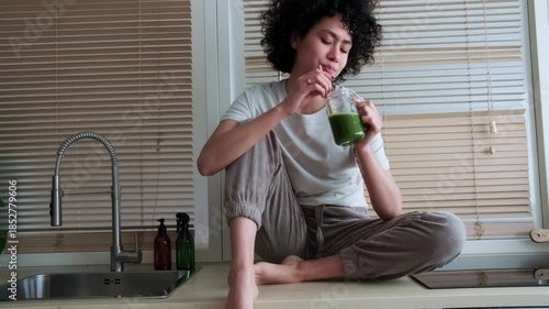 Beautiful woman enjoying green smoothie on kitchen counter