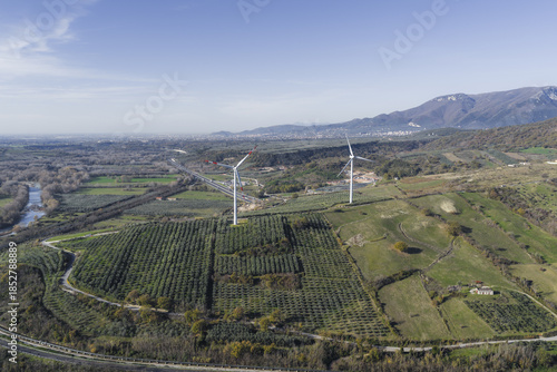 Aerial view of twin wind turbines standing tall against a backdrop of rolling hills, creating a stark contrast between modern technology and the natural landscape, Serre, Campania, Italy.