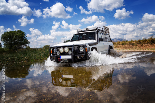 Off-road vehicle crossing shallow river in rural landscape