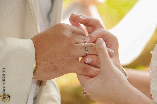 Bride placing the wedding ring on the groom's finger during an outdoor wedding ceremony. Engagement