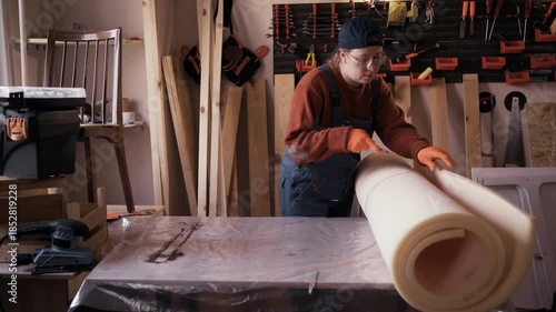 Female furniture restorer preparing foam padding for reupholstering vintage wooden chair in workshop