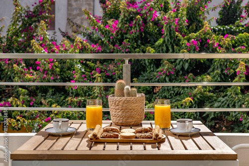 Mediterranean breakfast on a sunny balcony with fresh orange juice, coffee cups, pastries and cactus plant, relaxing summer travel and lifestyle concept