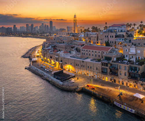 Aerial view of the ancient port city of Jaffa meeting the modern skyline of Tel Aviv under a fiery sunset, Tel Aviv-Yafo, Tel Aviv District, Israel.