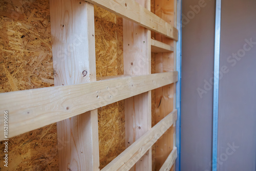 Close up interior wall framing shows planed softwood studs and noggins against OSB, with a metal channel on the right during rough in, shallow depth of field.
