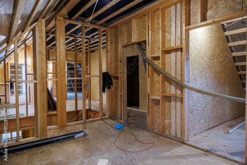 Принти на полотні Interior attic renovation shows stud framing, OSB sheathing, rafters, wires, and a large flexible duct  tools and cords indicate active work under even work lighting