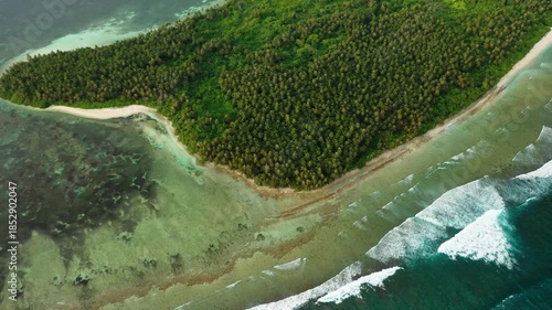 Aerial view of lush green vegetation meets the turquoise sea, white sand beaches, and foamy waves crashing gently, Maldives.