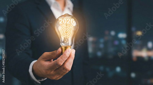 Businessman hand holding lightbulb with 2026. Concept of future business goals, new year, innovation, and strategic planning