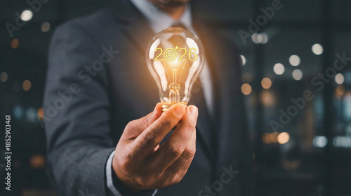 Businessman hand holding a glowing lightbulb with 2026 text and target