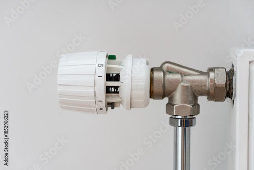 Close up view of thermostat of heating radiator with over white wall with copy space. Concept of heating season, setting a comfortable temperature at home and resources consumption.