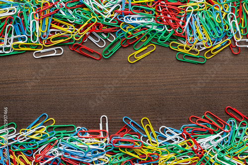 Top down photo of multicolored paper clips on the wooden table with copy space.