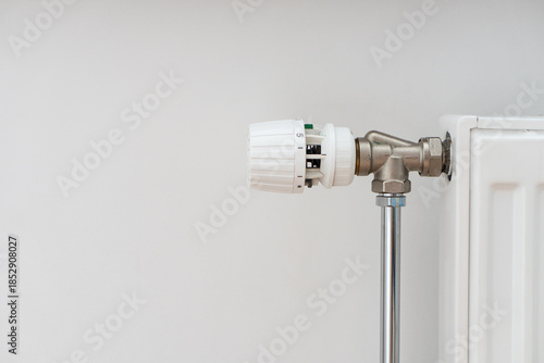 Close up view of modern heating radiator with thermostat in living room over white wall with copy space. Concept of heating season, setting a comfortable temperature at home and resources consumption.