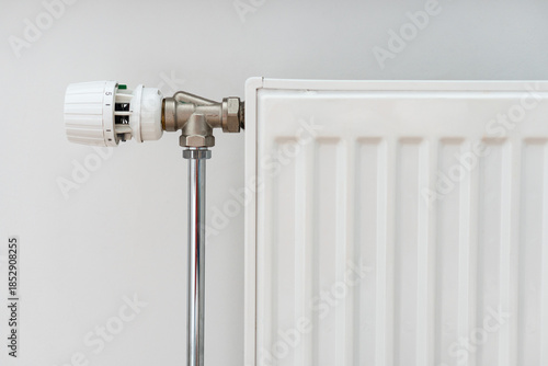 Close up view of modern heating radiator with thermostat in living room. Concept of heating season, setting a comfortable temperature at home and resources consumption.