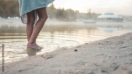 Φωτογραφία Person's bare feet wading into calm lake water at sunrise with morning mist