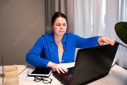 Remote employee beginning work from home routine. Focused woman turning on computer at home office. Modern work from home lifestyle