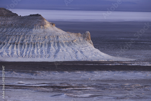 View of stark white cliffs edge a vast, flat expanse under a muted, dusky sky, creating a desolate yet beautiful landscape, Bozhira, Mangystau Region, Kazakhstan.