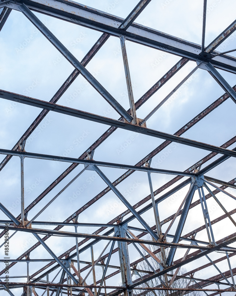 Fototapeta premium Metal framework of a disassembled building under a cloudy sky in an urban area