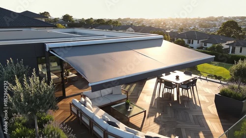 High aerial drone shot moving slowly over a luxurious suburban rooftop patio featuring a fully extended gray modern retractable awning providing shade destination, drone, structure