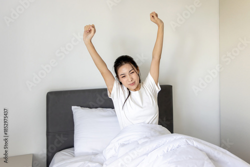 Beautiful sleepy Asian woman waking up in bed, stretching her arms in the morning. Young pretty female sleeping on comfortable bed and trying to wake up. A woman stretching lazily after waking up.
