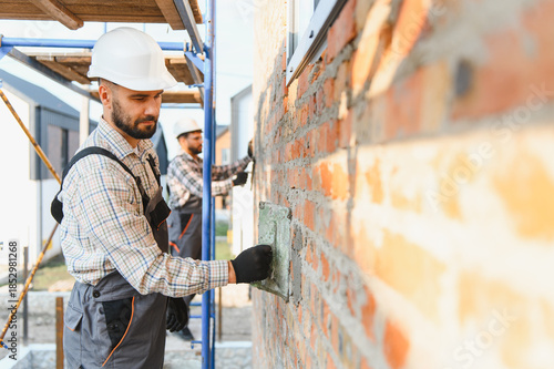 Construction workers bricklaying house wall, applying mortar