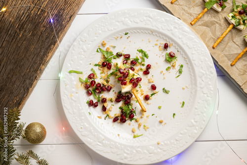 Preparing tree shaped brie cheese appetizers with pomegranate, walnuts, cilantro and a pretzel stick