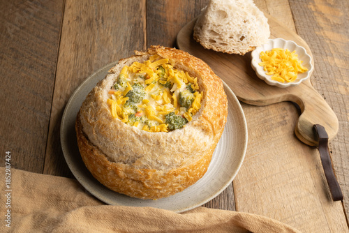 Broccoli cheddar soup in a sourdough bread bowl on wooden table with brown napkin and antique spoon